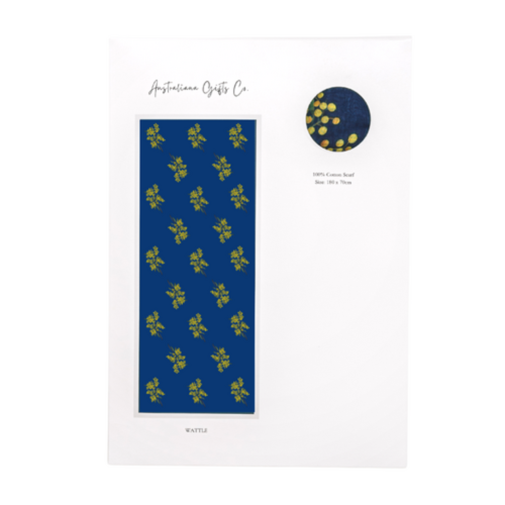a lightweight cotton scarf that has a navy blue background and bunches of yellow Wattle flowers with green leaves. The scarf is packaged in a white envelope with information about the Wattle flower.