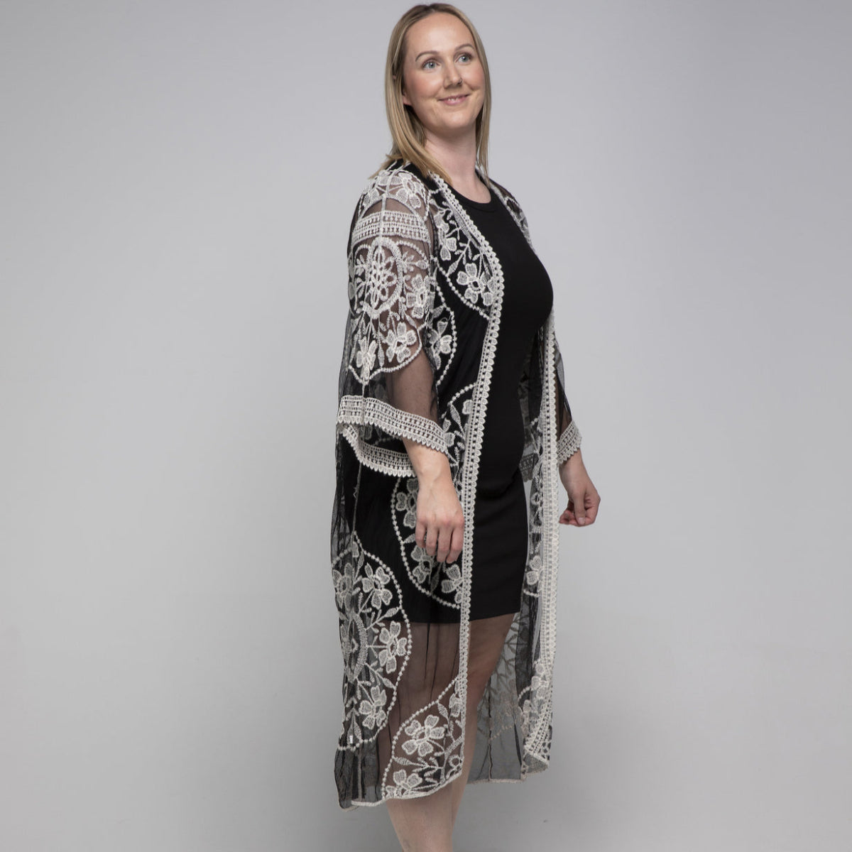 Woman wearing a black kimono with a white lace cover-up against a gray background