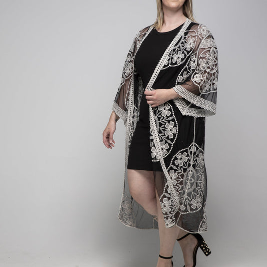 Woman wearing a black dress with a white lace cover-up against a gray background