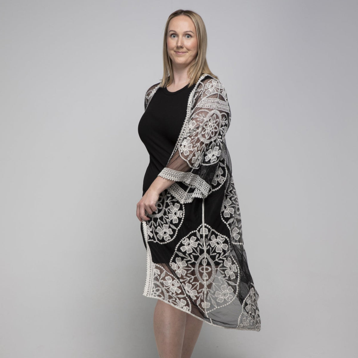 Woman wearing a black kimono with a white lace cover-up against a gray background