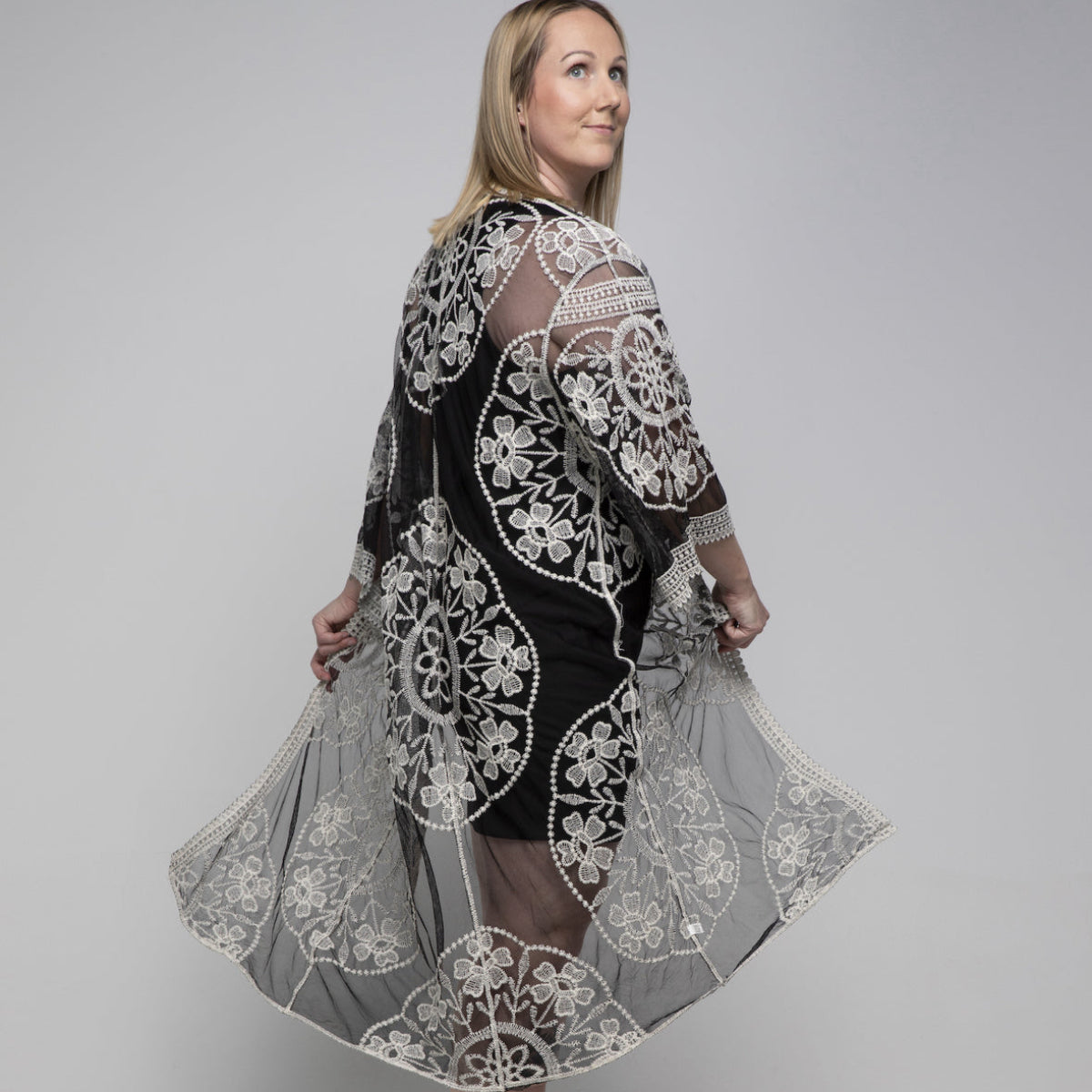 Woman wearing a black kimono with white lace details on a gray background