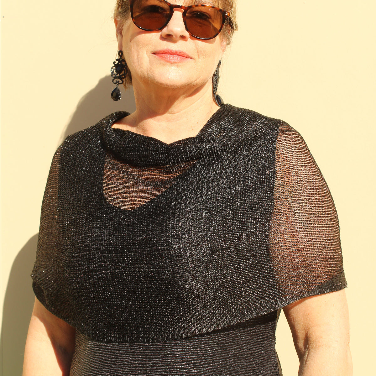 a lady wearing sunglasses, a black evening dress and a sparkly black shawl that has glitter and tassels