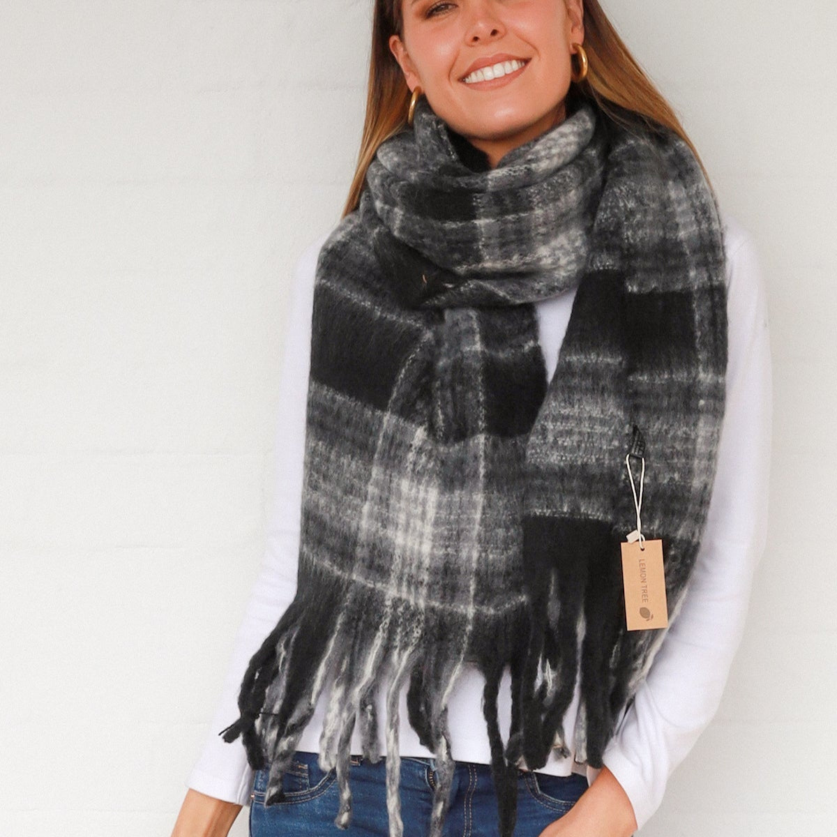 Woman wearing a black and gray plaid scarf with chunky tassels against a grey background.