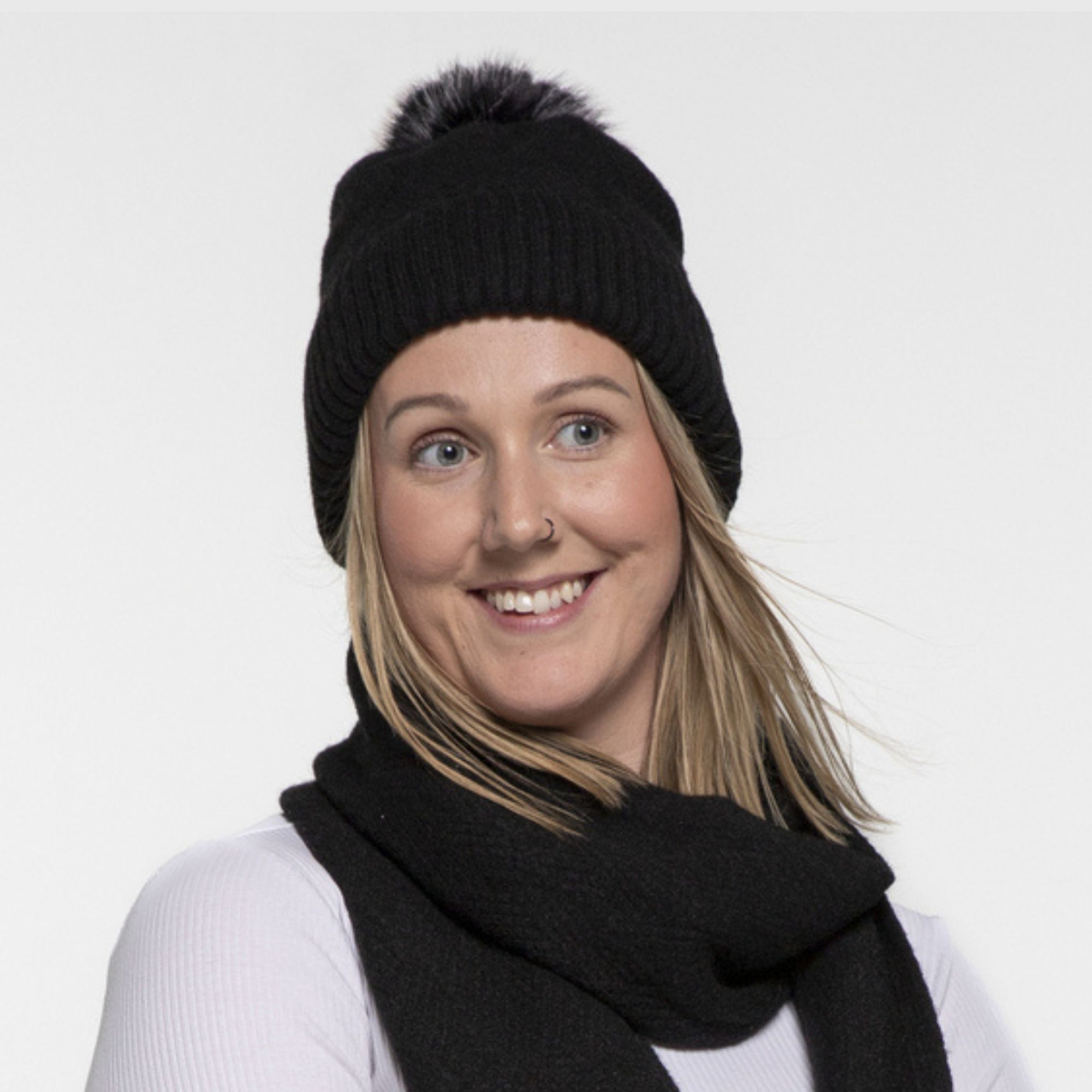 Person wearing a black knit beanie with a pom-pom and black scarf on a white background