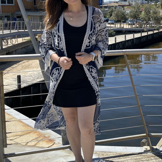 Woman wearing a black dress and patterned cardigan by a waterfront