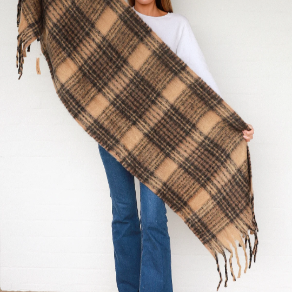 Woman holding a large plaid scarf against a white wall