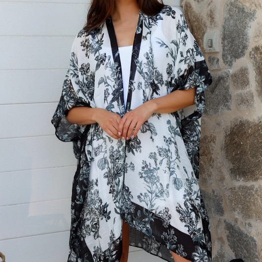 Woman wearing a black and white floral kimono against a stone wall.