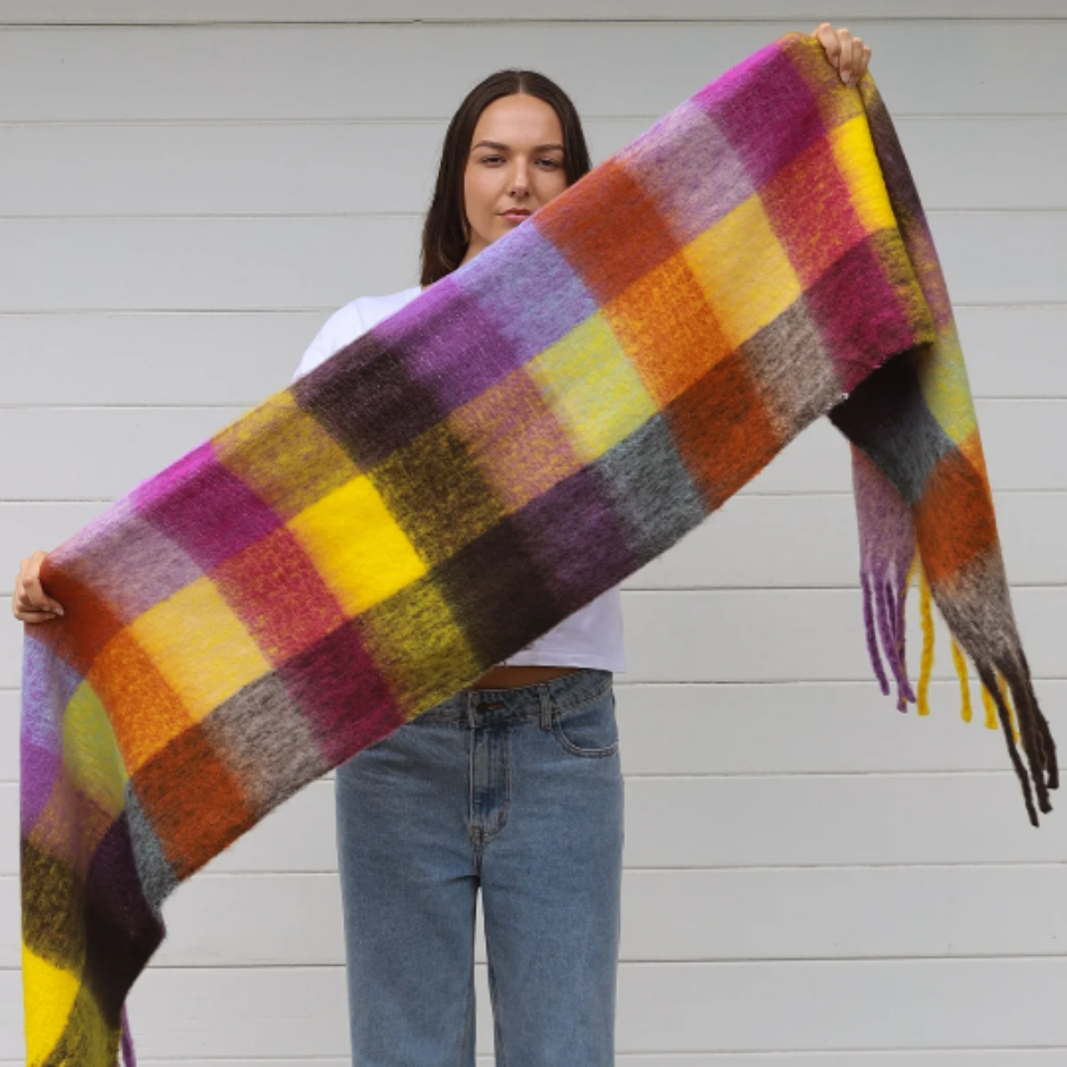 Person holding a colorful plaid scarf in front of a white wall
