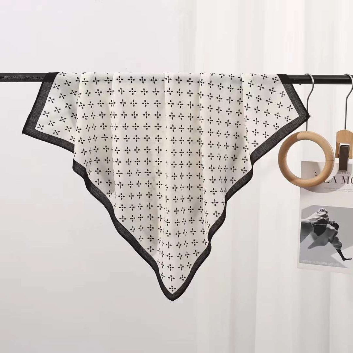 Black and white patterned scarf hanging on a rack against a white curtain.