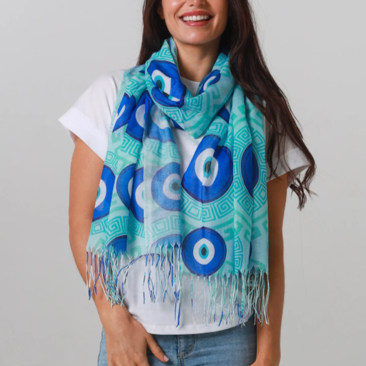 Woman wearing a blue and green Evil Eye patterned scarf on a plain background
