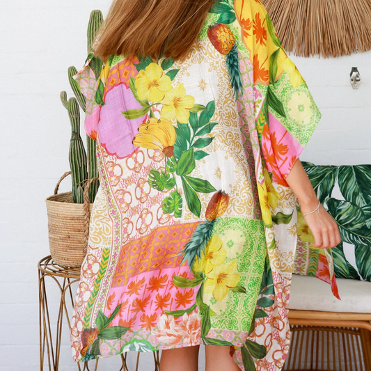 Woman wearing a colorful floral kimono in a room with a cactus and woven chair.