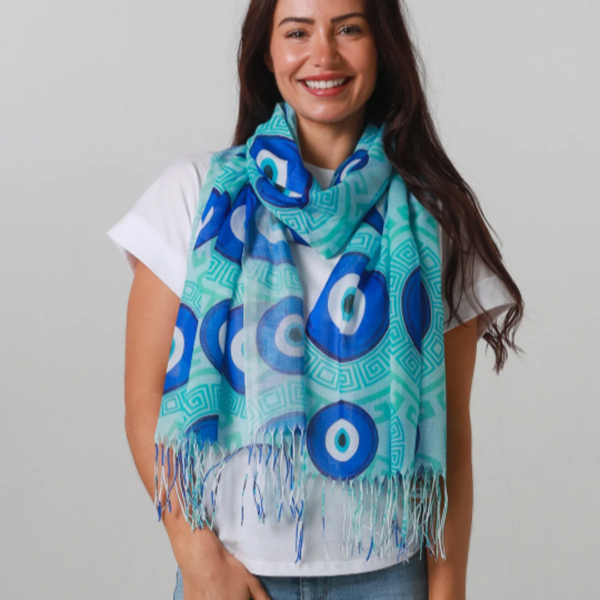 Woman wearing a blue and green patterned scarf with fringes on a plain background