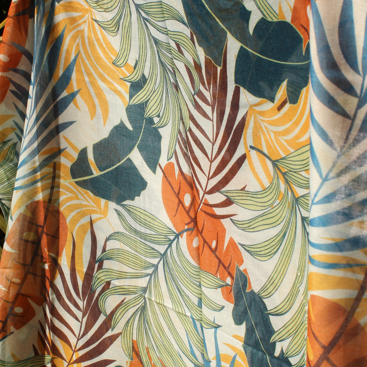 Tropical leaf patterned scarf held up against a dark background