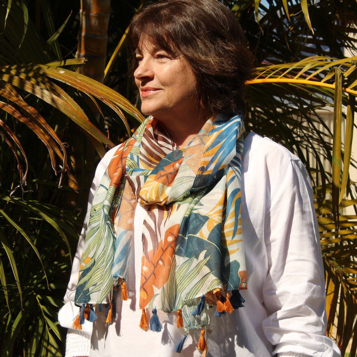 Person wearing a colorful floral scarf and a white top with palm trees in the background