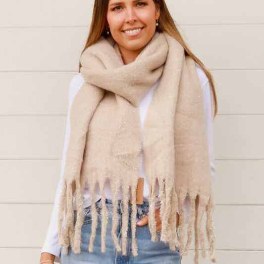 Woman wearing a beige scarf with gold glitter and tassels against a light background