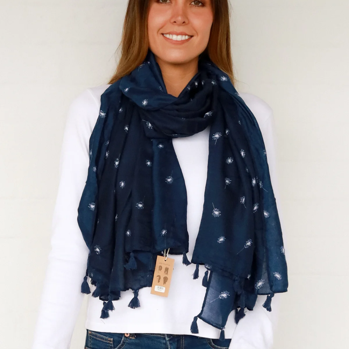 Woman wearing a navy blue scarf with white patterns and tassels, standing against a plain background.