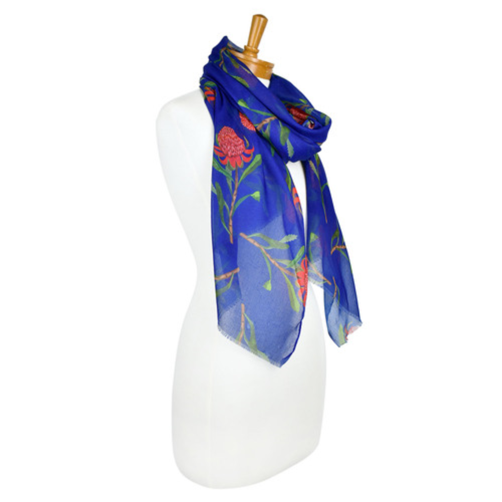 a lightweight cotton scarf that has a navy blue background and bright pink Waratah flowers with green stems and leaves. The scarf is draped around a mannequin and shows the side view.