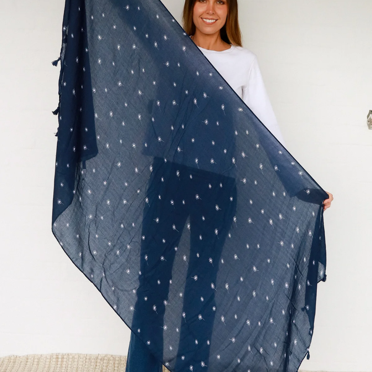 Woman holding a large navy blue scarf with white dandelion pattern against a plain background