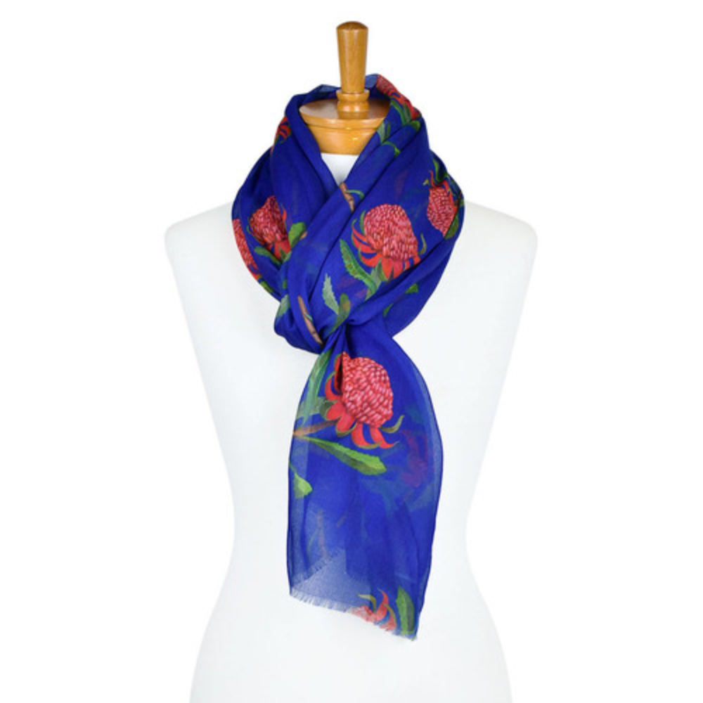 a lightweight cotton scarf that has a navy blue background and bright pink Waratah flowers with green stems and leaves. The scarf is tied around a mannequin.