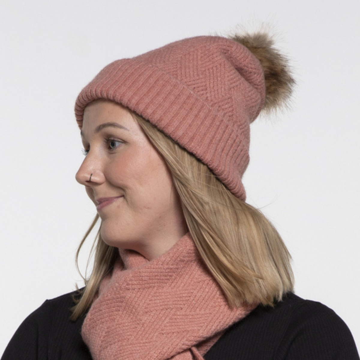 Person wearing a pink knit beanie with a pom-pom and matching scarf on a white background