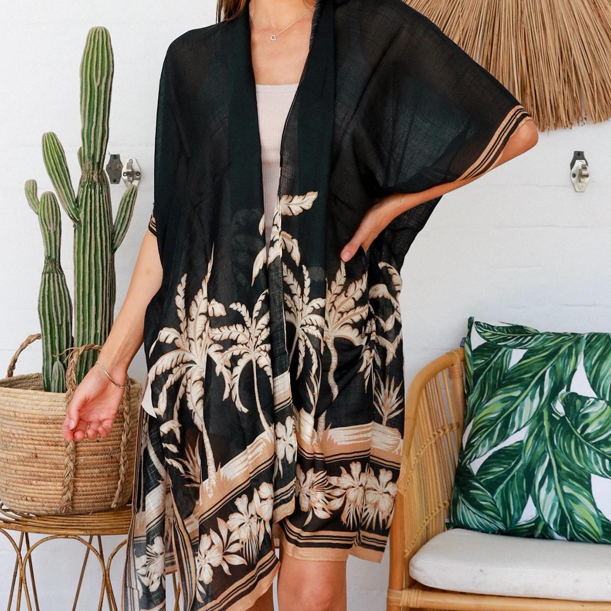 Woman wearing a black floral kimono in a tropical-themed room with a cactus and woven chair.