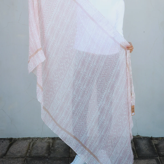 Woman holding a white and taupe brown scarf against a plain background