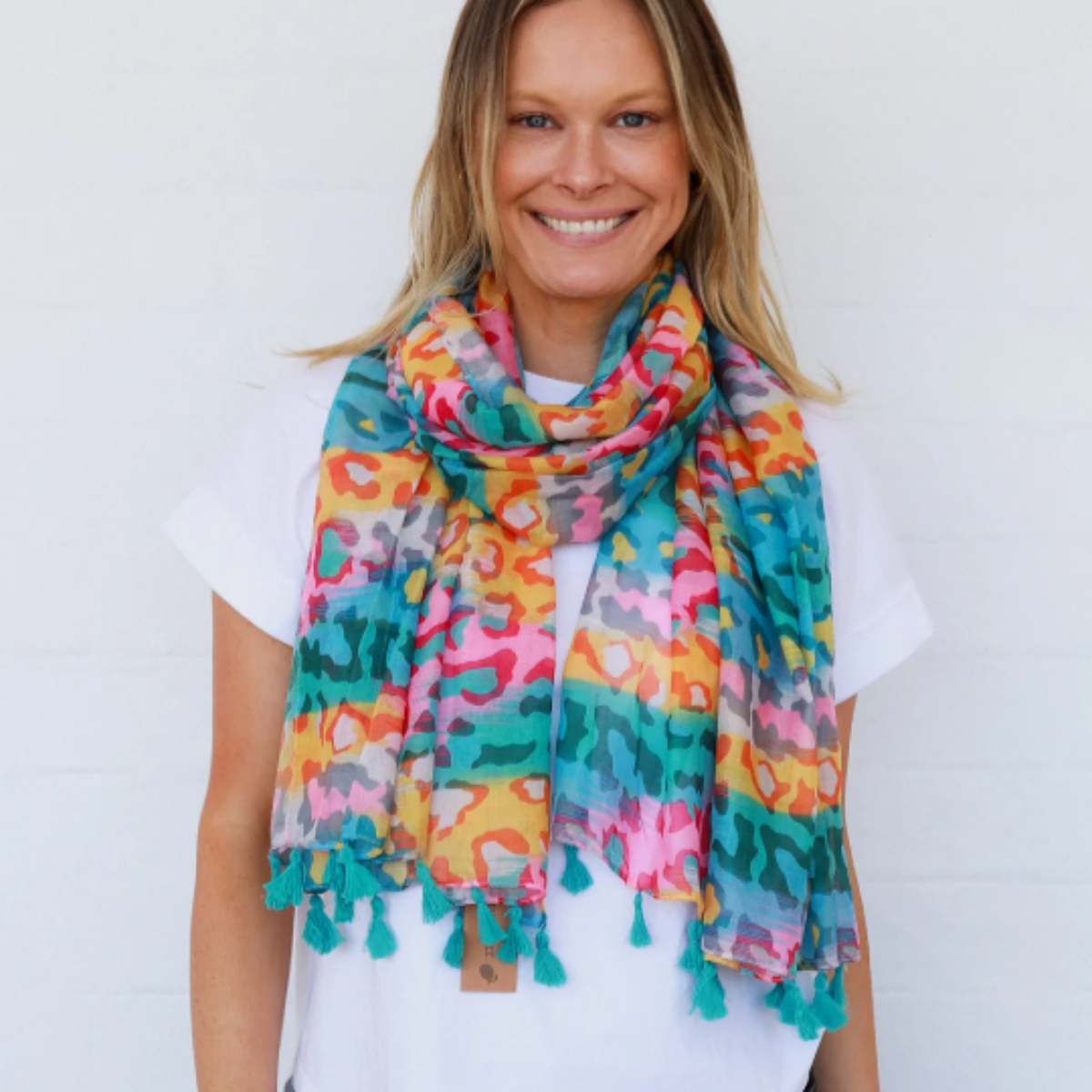 a lady wearing a brightly coloured leopard print scarf that is finished with turquoise blue tassels.