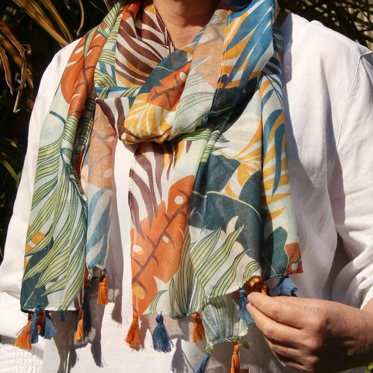 Person wearing a colorful floral-patterned scarf among palm leaves