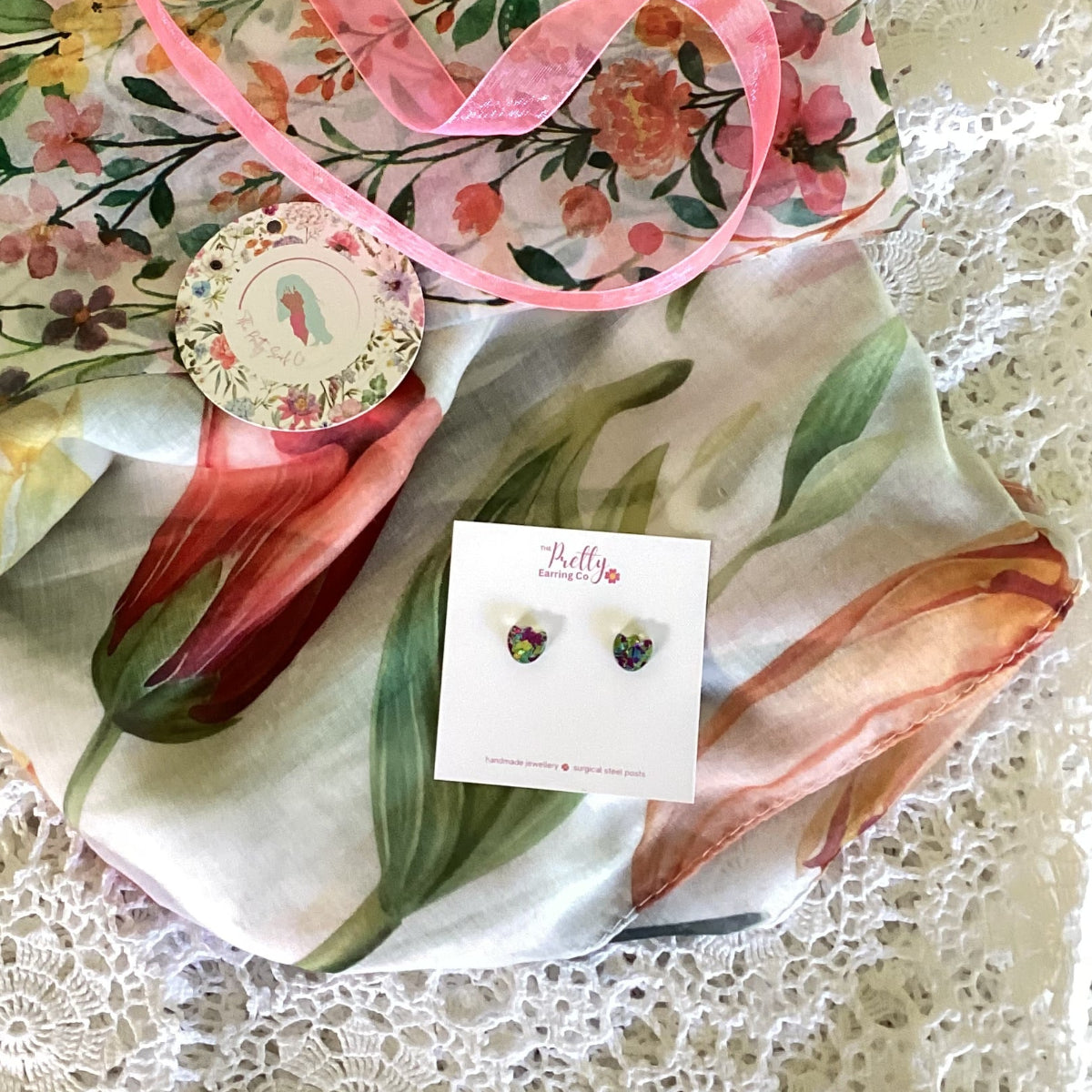 Floral scarf with a pink ribbon and earrings on a textured surface