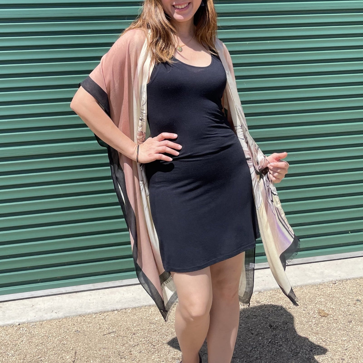 Woman wearing a black dress with a beige cardigan in front of a green metal shutter.
