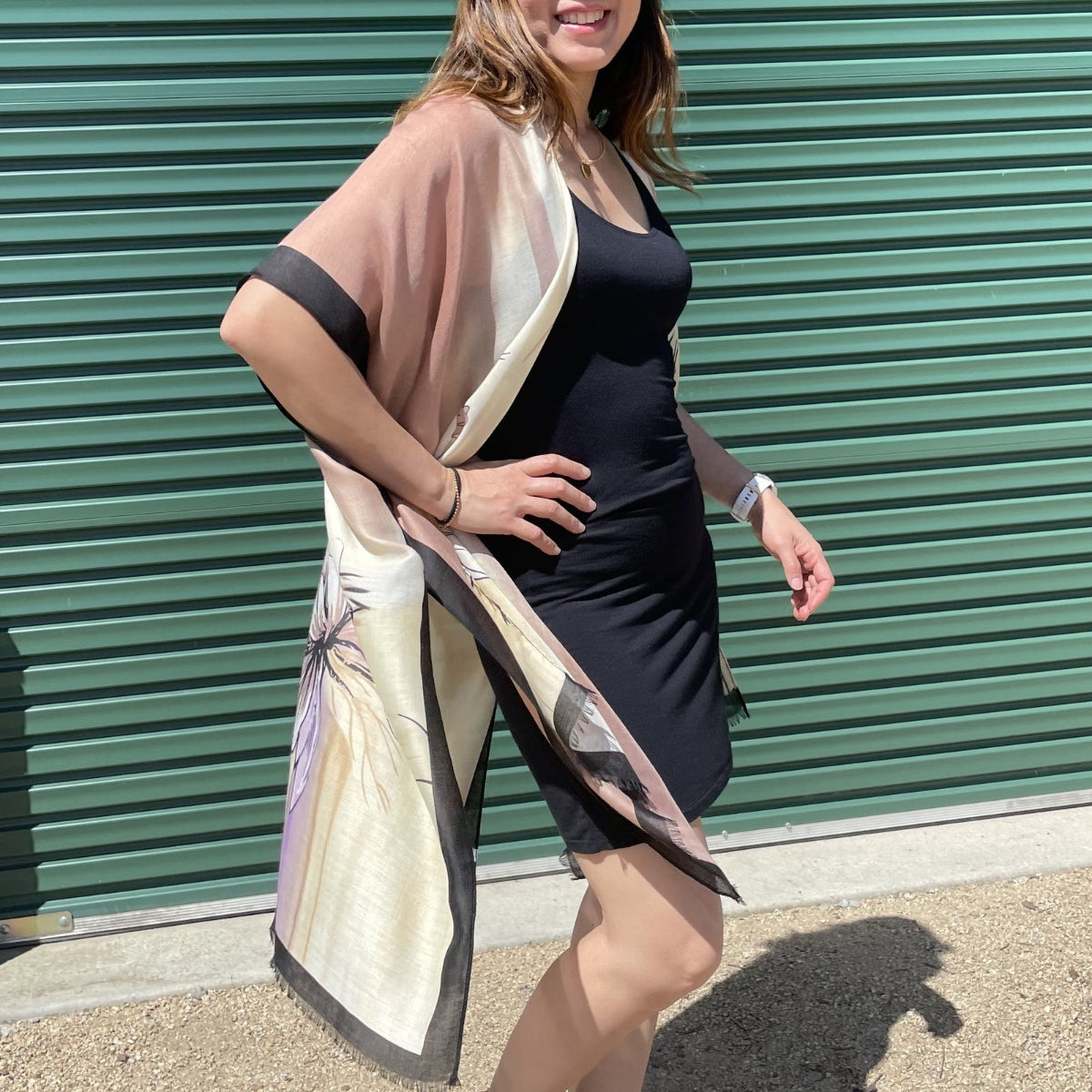 Woman wearing a black dress with a sheer beige cardigan in front of a green metal shutter.