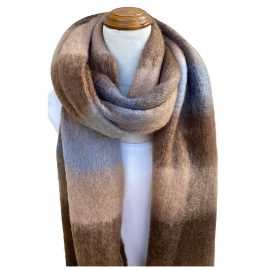 A soft, fuzzy scarf with a large gradient block pattern in shades of brown, beige, and muted blue-gray, draped on a white mannequin torso with a wooden cap.