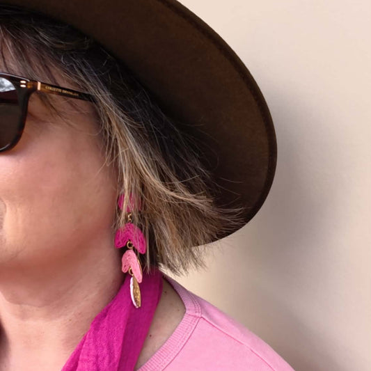 a side view of a woman wearing a hat and pink dangle earrings