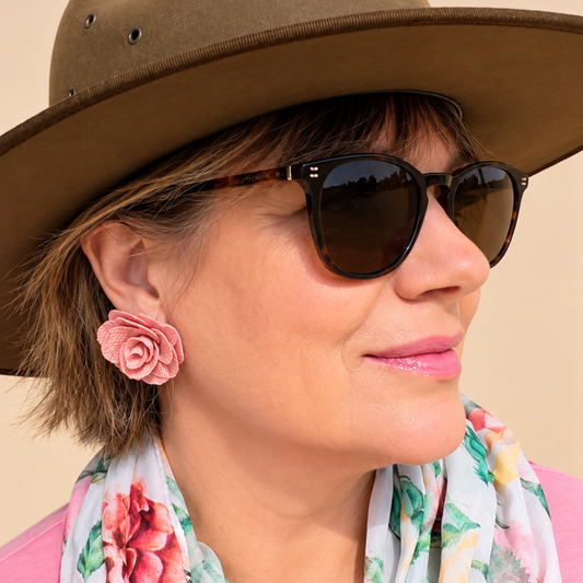 a woman wearing a hat, sunglasses, pink earrings in the shape of roses and a floral scarf