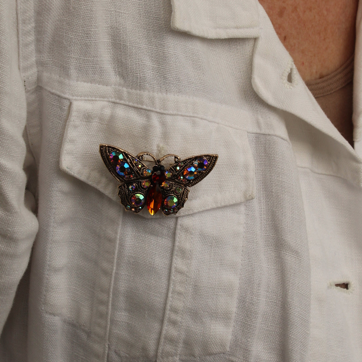 A close-up of a person wearing a white linen button-up shirt, featuring a decorative butterfly brooch pinned to the chest pocket.
