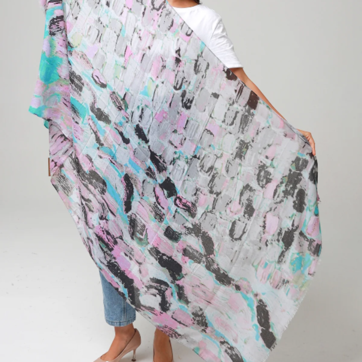 Woman holding a large, colorful scarf with abstract patterns on a plain background