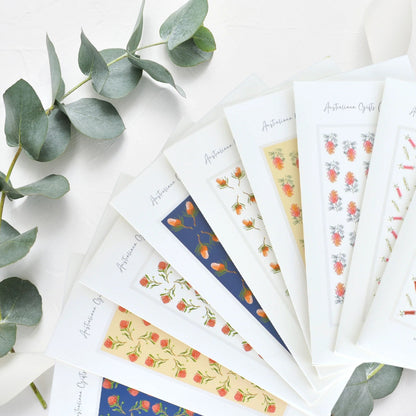 Set of packaged scarves with floral designs on a white surface with eucalyptus leaves.