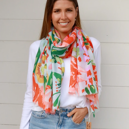 Woman wearing a colorful floral scarf, white shirt, and blue jeans against a light background