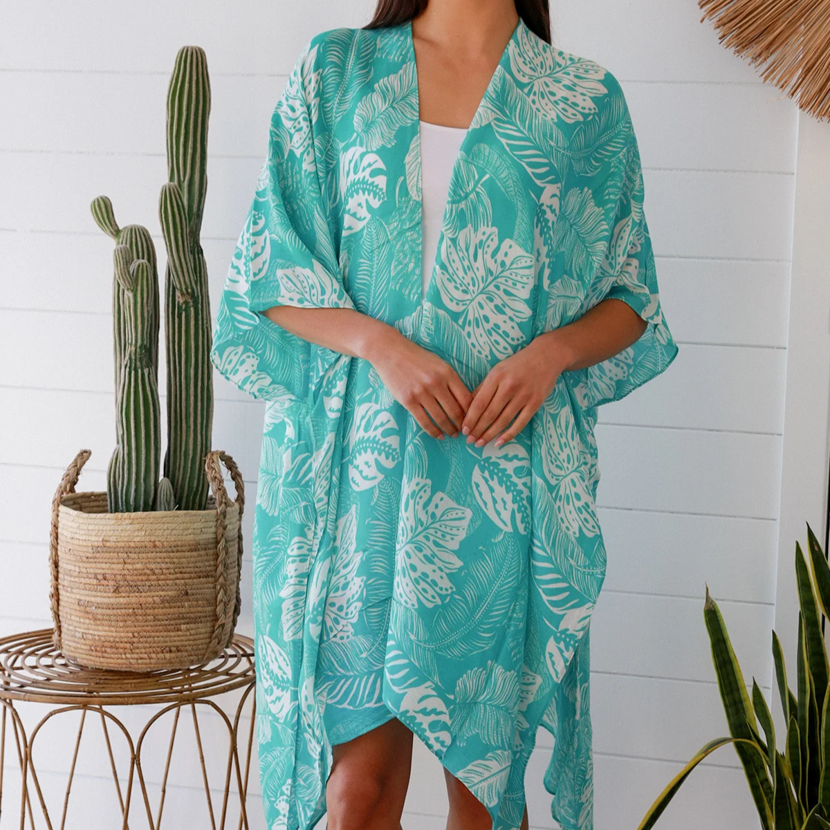 Woman wearing a turquoise floral kimono in a home setting with plants.