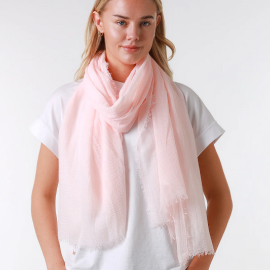 Woman wearing a light pink scarf, white shirt, and blue jeans on a white background