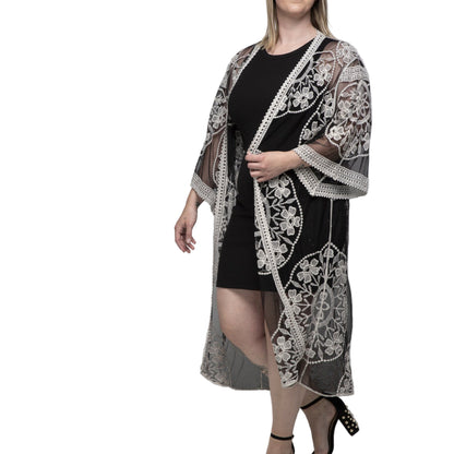 Woman wearing a black dress with a white lace cover-up against a gray background