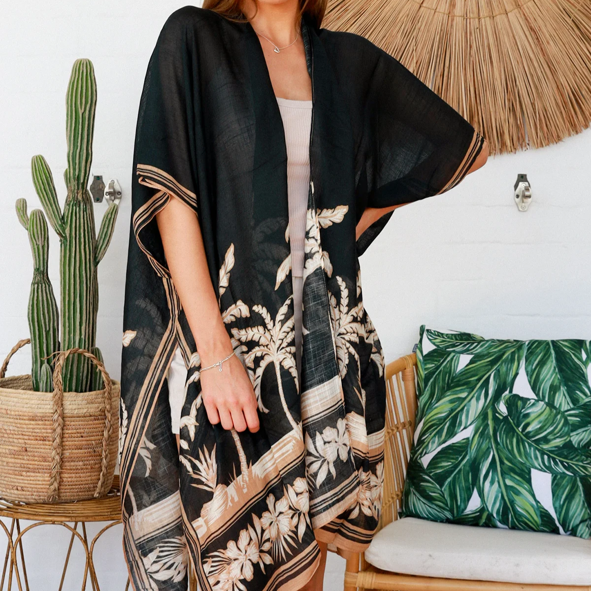 Woman wearing a black floral kimono in a tropical setting with a cactus and palm leaves.
