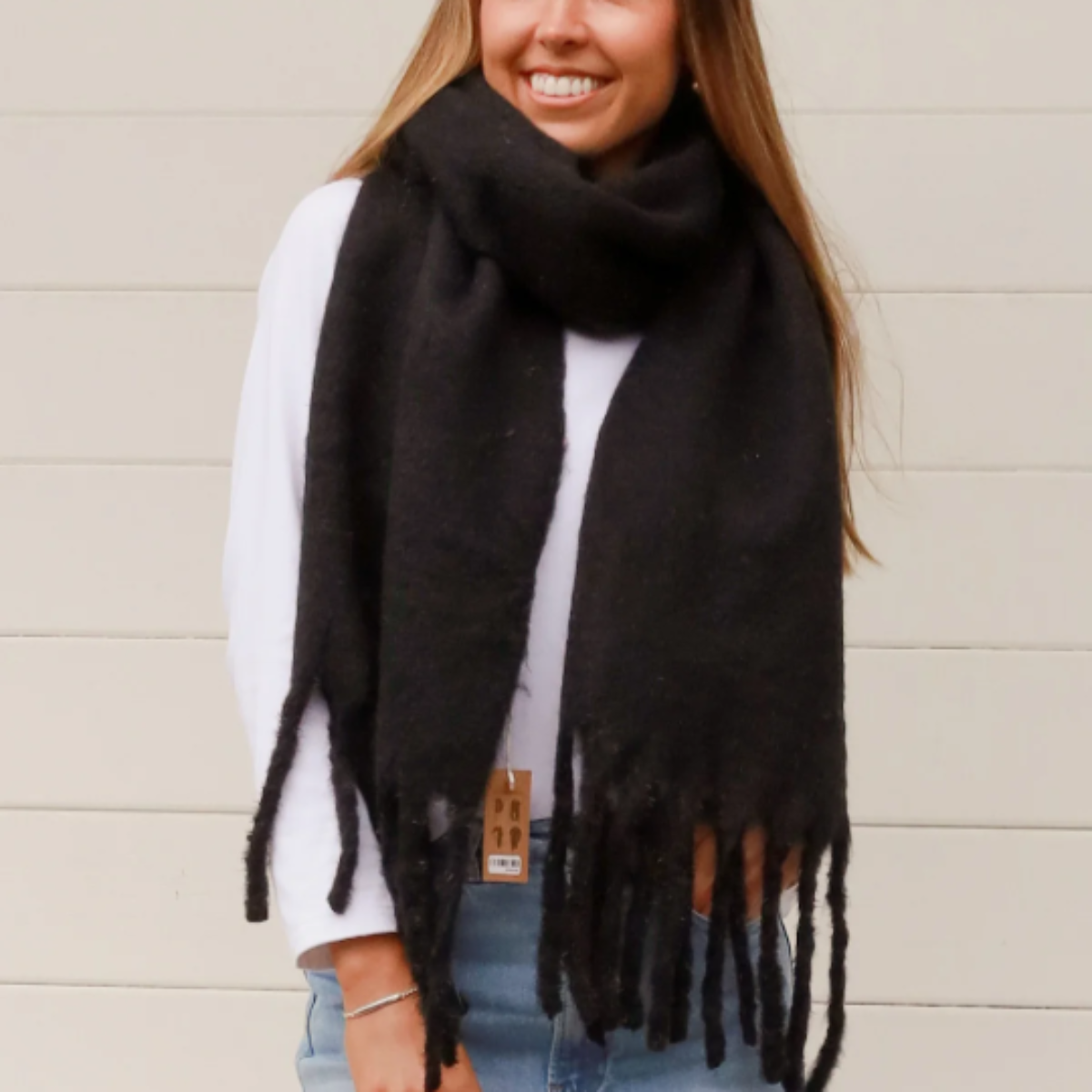 Woman wearing a black scarf with tassels against a beige wall