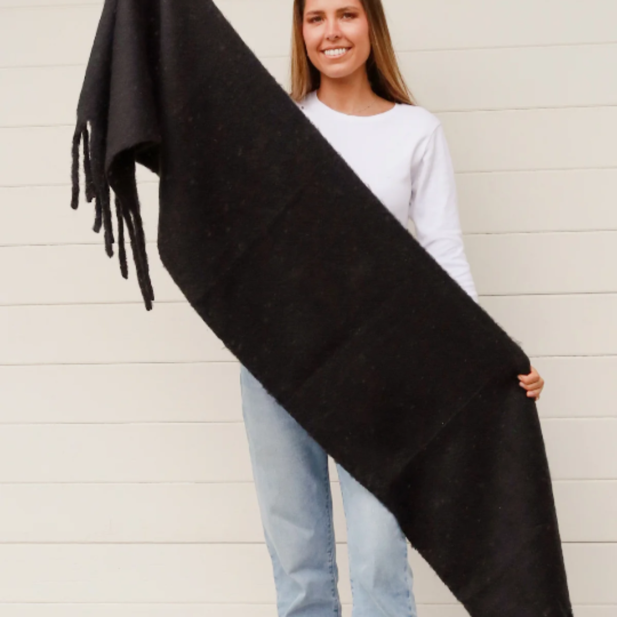 Woman holding a black scarf with fringes against a light background