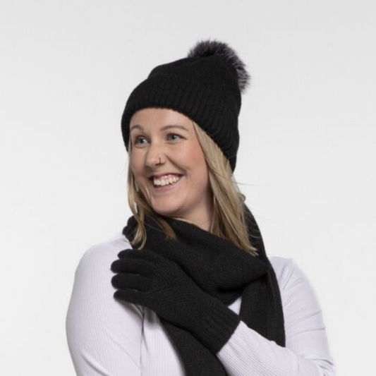 Lady wearing a black knit beanie with a pom-pom and matching scarf on a white background