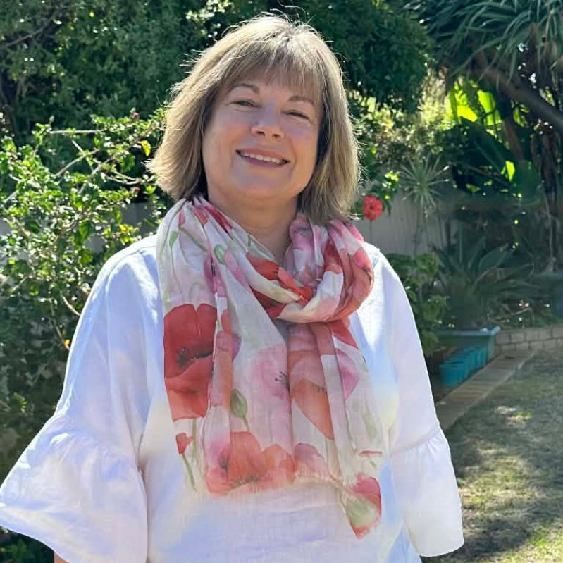Woman standing outdoors with greenery and palm trees in the background and wearing a pink and red floral scarf