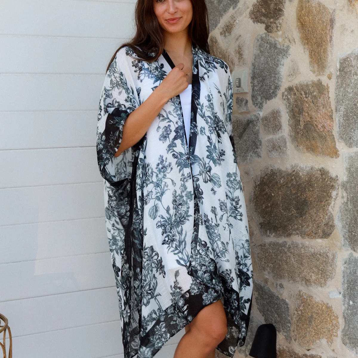 Woman wearing a floral kimono standing against a stone wall.