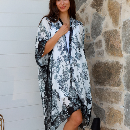 Woman wearing a floral kimono standing against a stone wall.