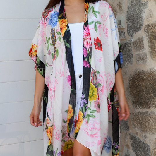 Woman wearing a colorful floral kimono over a white shirt against a stone wall.