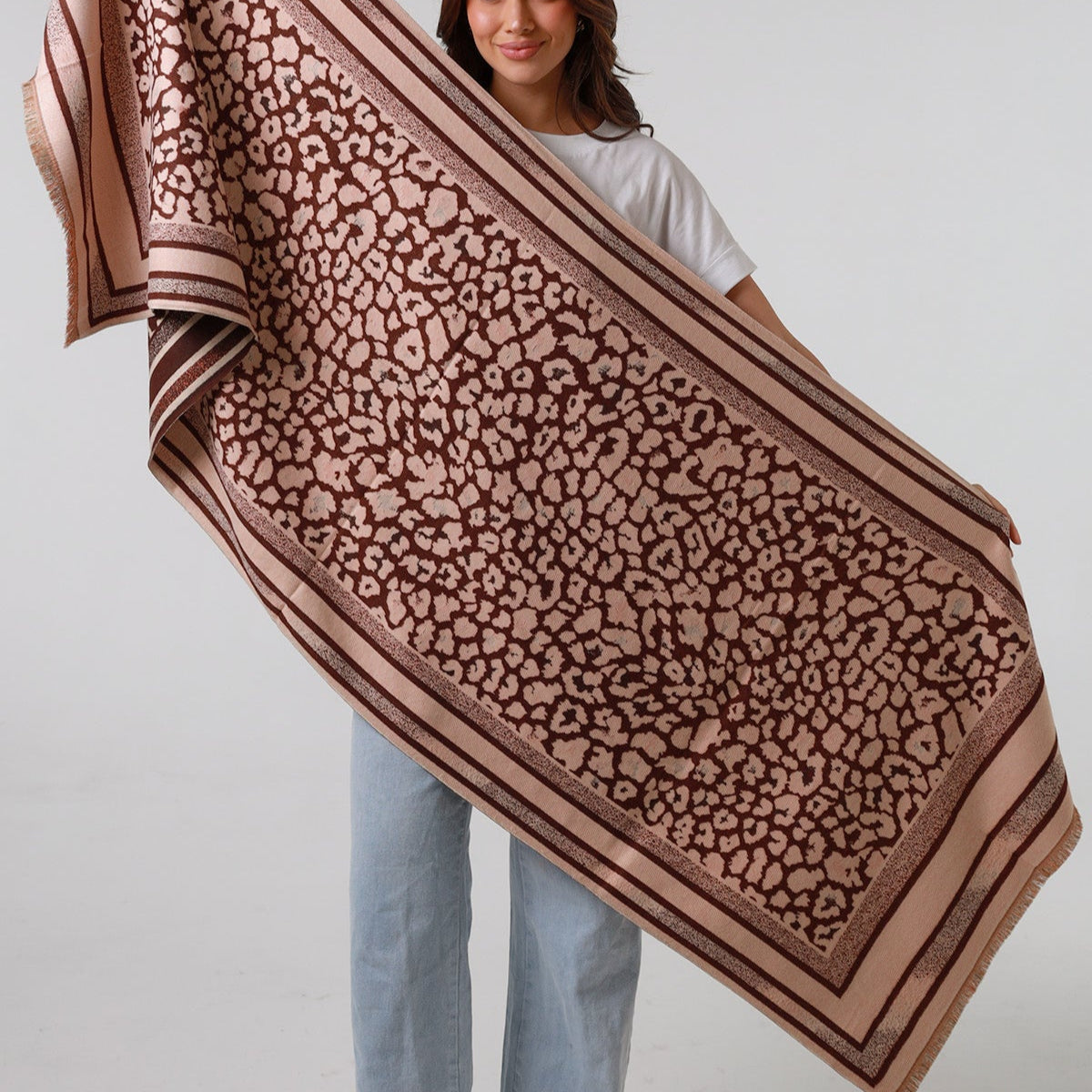 Woman holding a large brown leopard print scarf against a white background